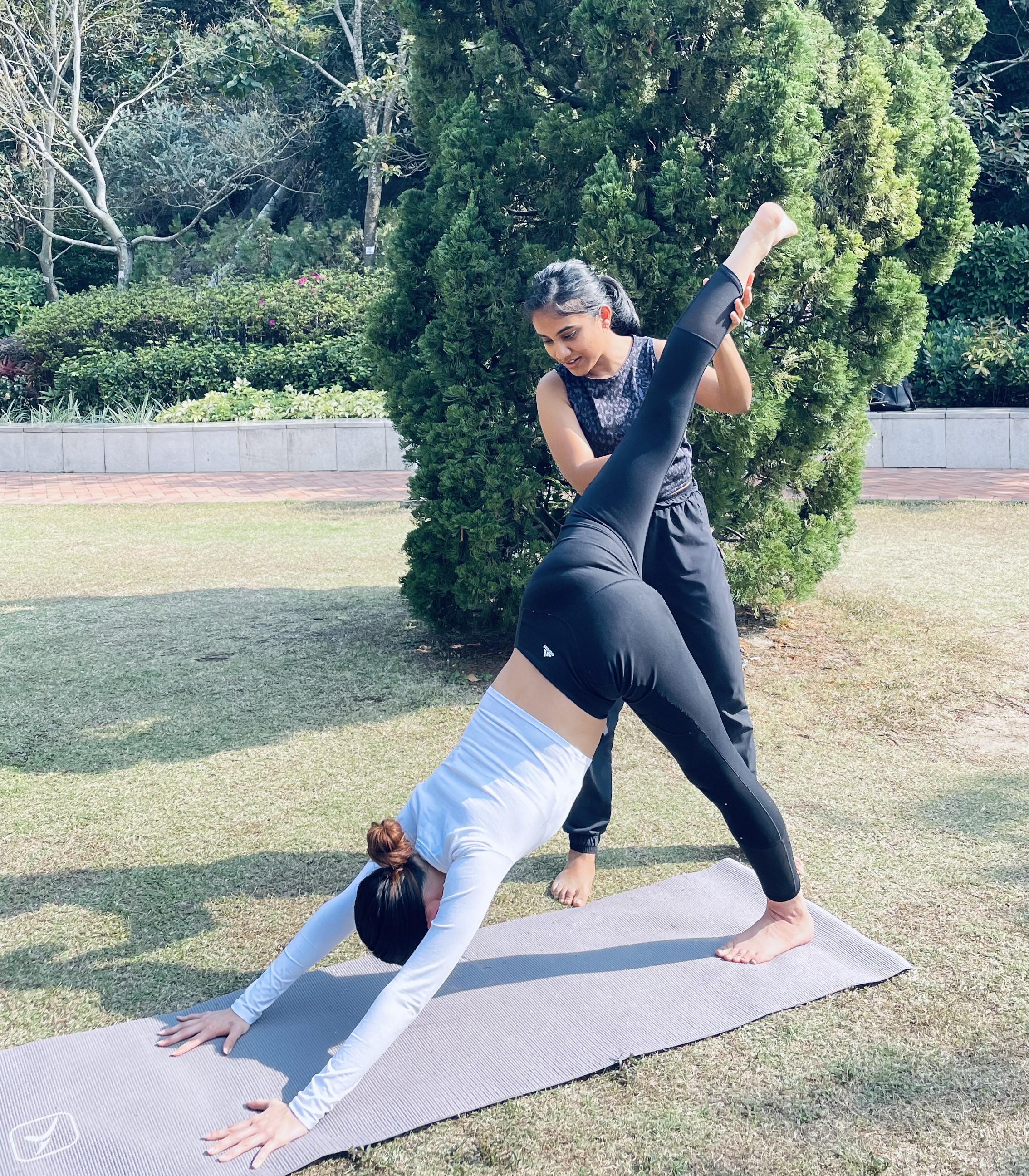 One person teaching a yoga pose to another on their yoga mats in a open place